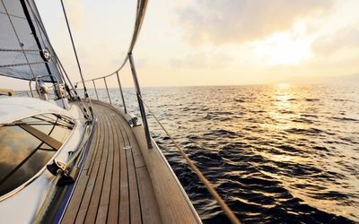 View over the wooden deck of a sailboat looking out at the open ocean during a moody sunset.